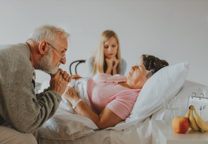 woman sitting and eldery man, with elderly woman in bed